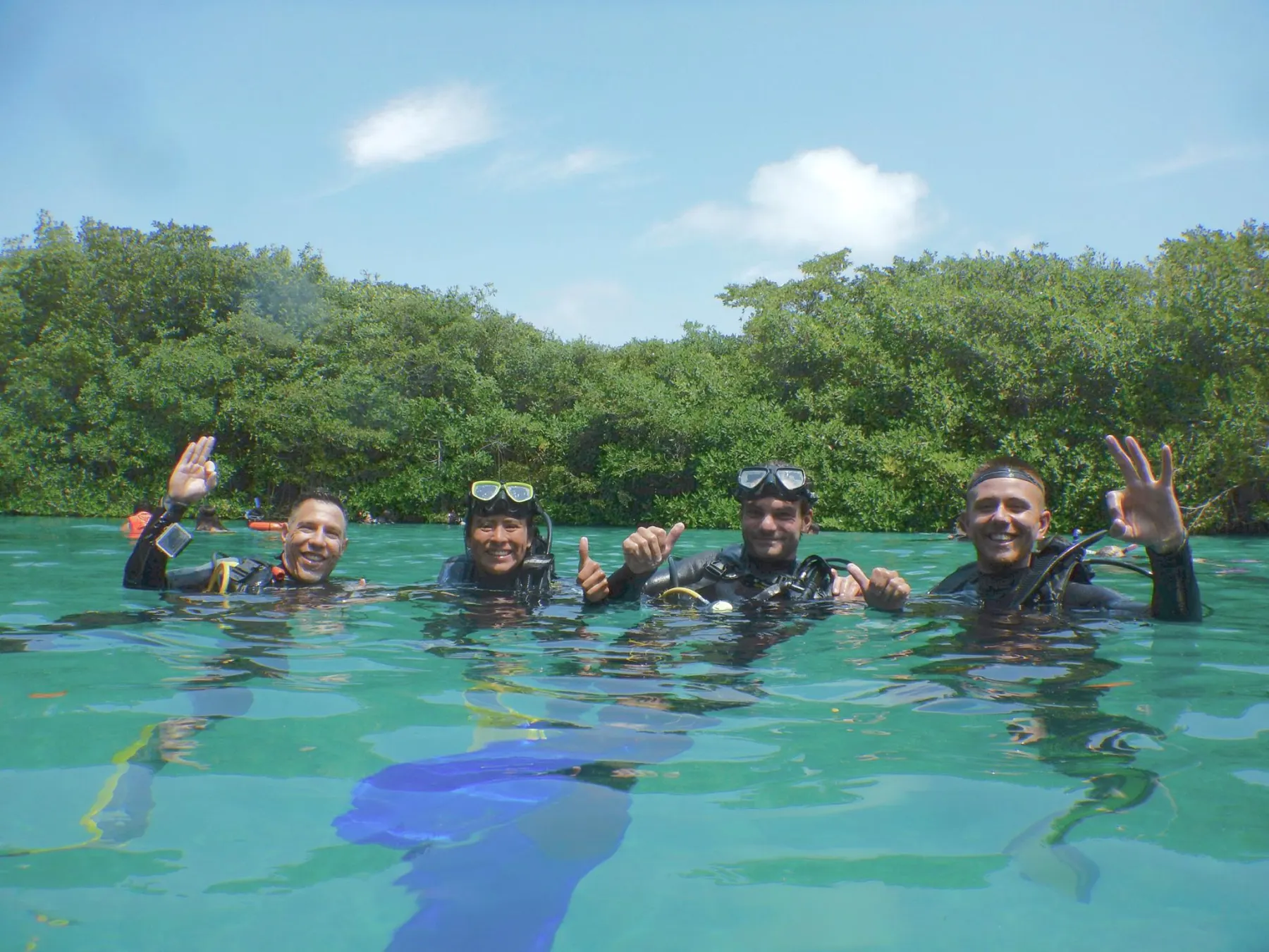 Four divers smiling at the surface in clear green cenote water