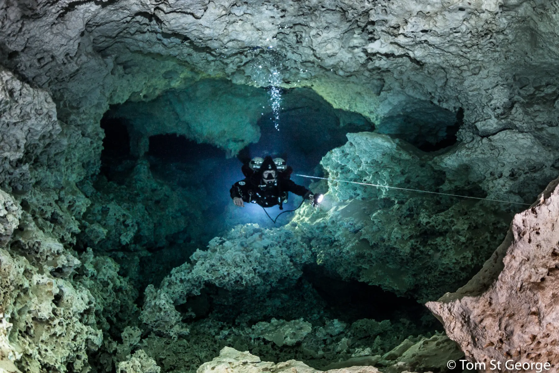 Diver with a light in a blue cenote cavern