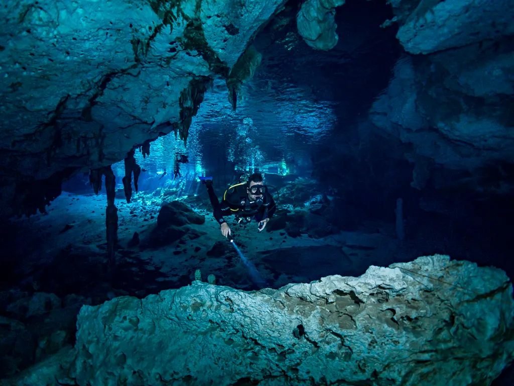 Diver swimming beneath a low cavern ceiling in Dos Ojos