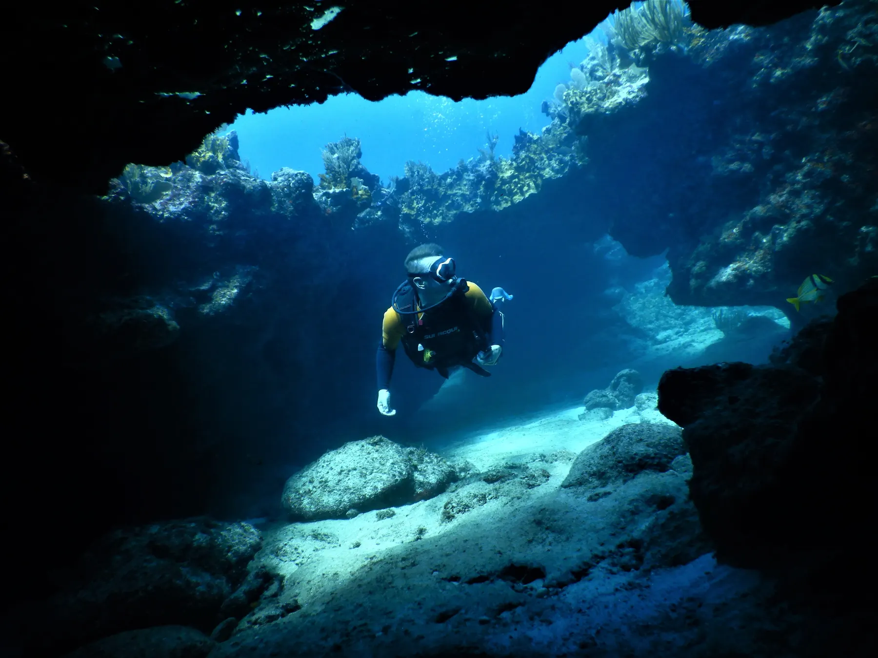 Diver passing through a shaded reef swim-through