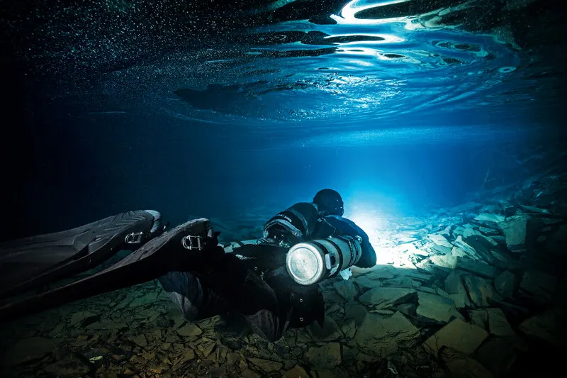 Sidemount diver with a light over a rocky cave floor